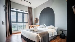 A modern hotel room with a large bed, a view of the city, and a round mirror on the wall.