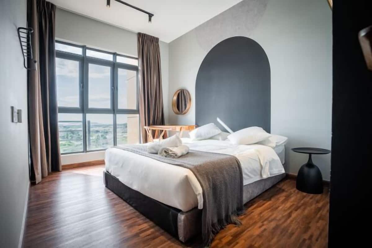 Une chambre d’hôtel moderne avec un grand lit, une vue sur la ville et un grand miroir rond au mur.