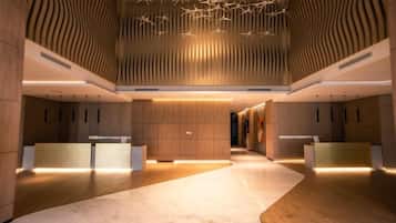A modern hotel lobby with a central reception desk, wooden paneling on the walls, and a marble floor.