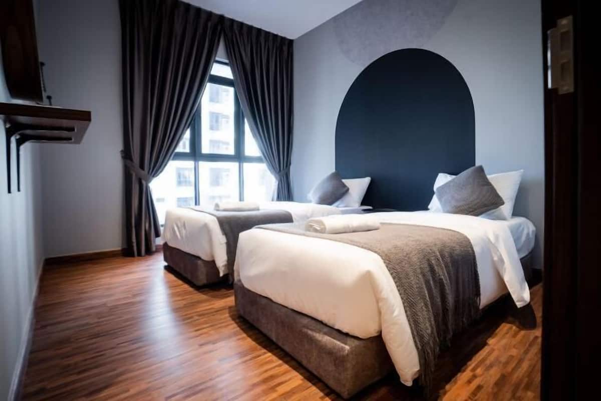 Une chambre d’hôtel avec deux lits, un plancher en bois, une grande fenêtre avec des rideaux et un mur d’accent de couleur foncée.