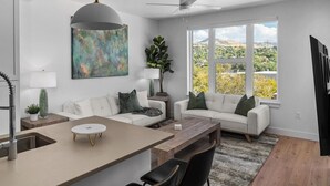 Uma sala de estar moderna com um sofá branco, uma mesa de centro de madeira e uma janela grande que oferece vista para o exterior.