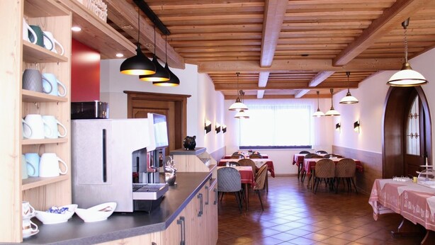 Un restaurante con vigas de madera, una zona de bar con una máquina de café y mesas dispuestas para comer.