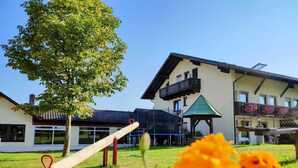 Un edificio con balcón, parque infantil y una estructura con techo verde.