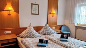 Habitación de hotel con dos camas, cada una con ropa de cama y toallas estampadas, una mesita de noche, una silla y lámparas fijadas a la pared.