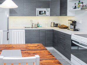 Une cuisine moderne avec des meubles gris, un plan de travail blanc, un four à micro-ondes, une machine à café et une cuisinière.