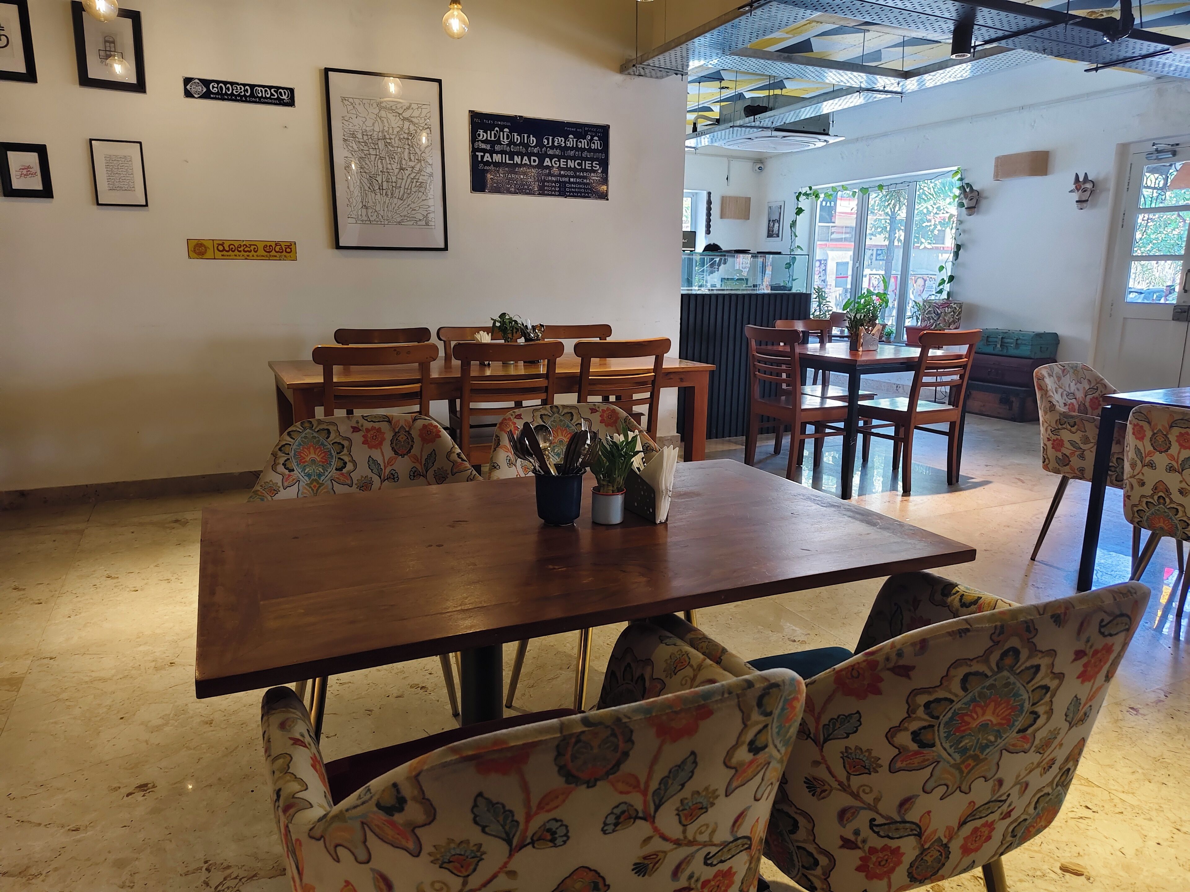 A dining area with wooden tables and chairs, framed artwork on the walls, and a view of the outside through large windows.