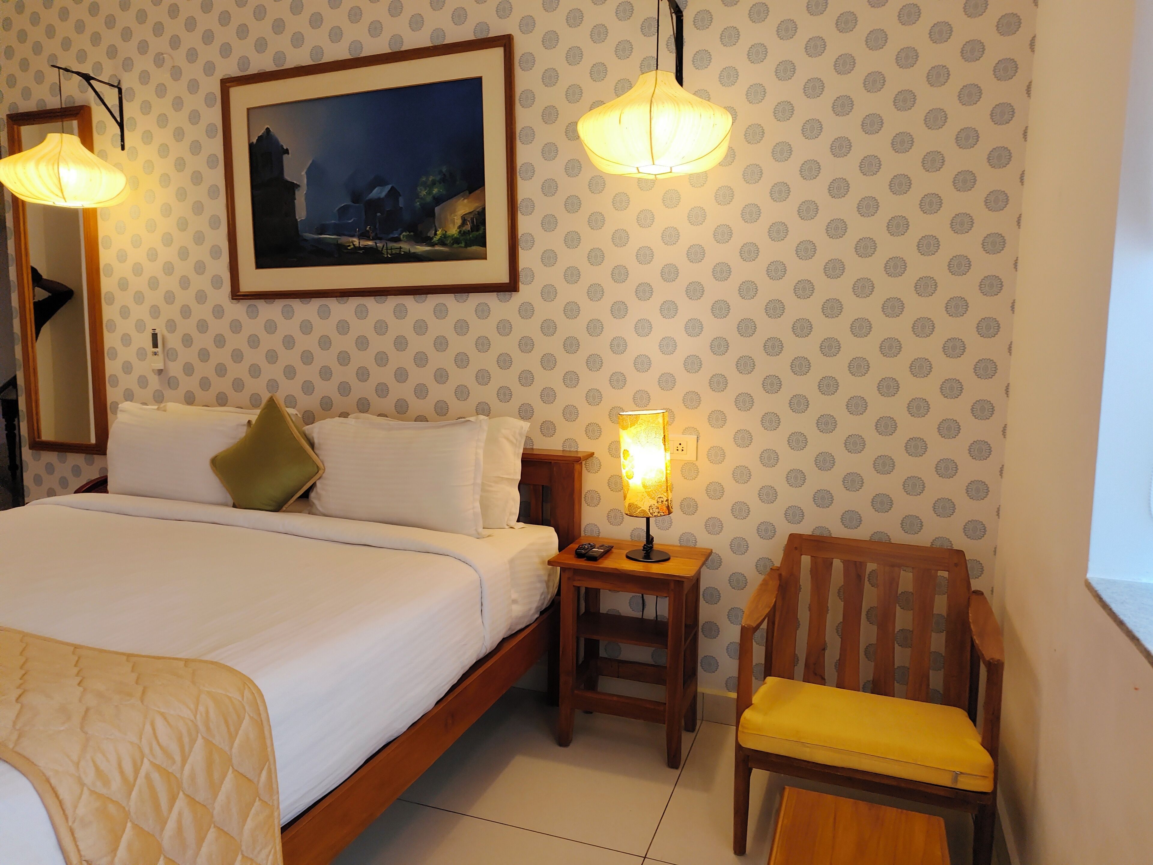 Une chambre d’hôtel avec un lit, une chaise, une table de chevet, une lampe, un tableau et un papier peint à motifs.
