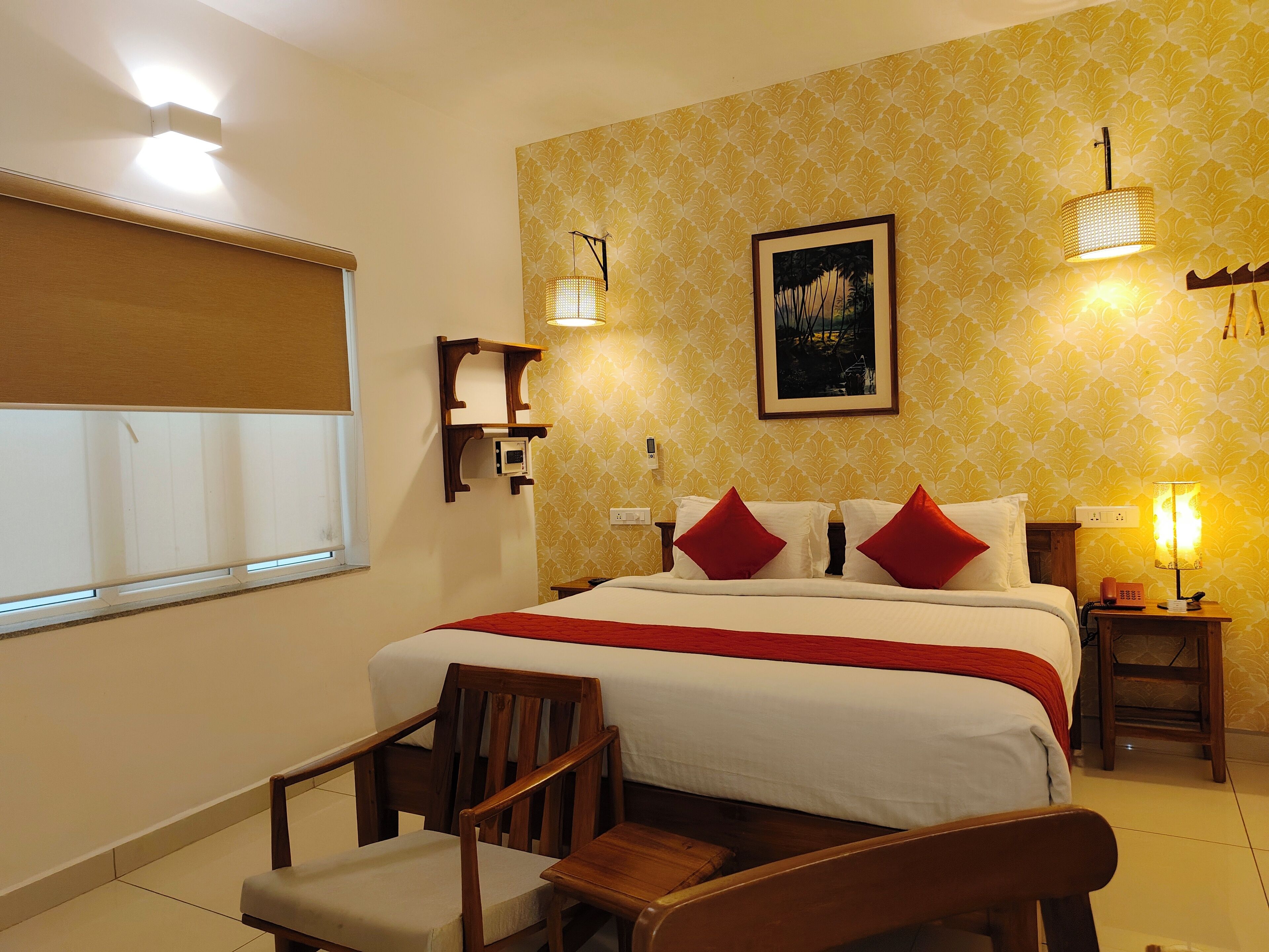 Ein Hotelzimmer mit einem Bett, zwei Nachttischen, einem Sessel, einem Fenster mit Jalousien und einer Wand mit ornamentalem Wandpapier.
