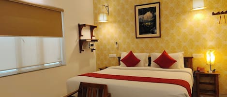 A hotel room with a bed, two bedside tables, a chair, a window with blinds, and a wall with a patterned wallpaper.