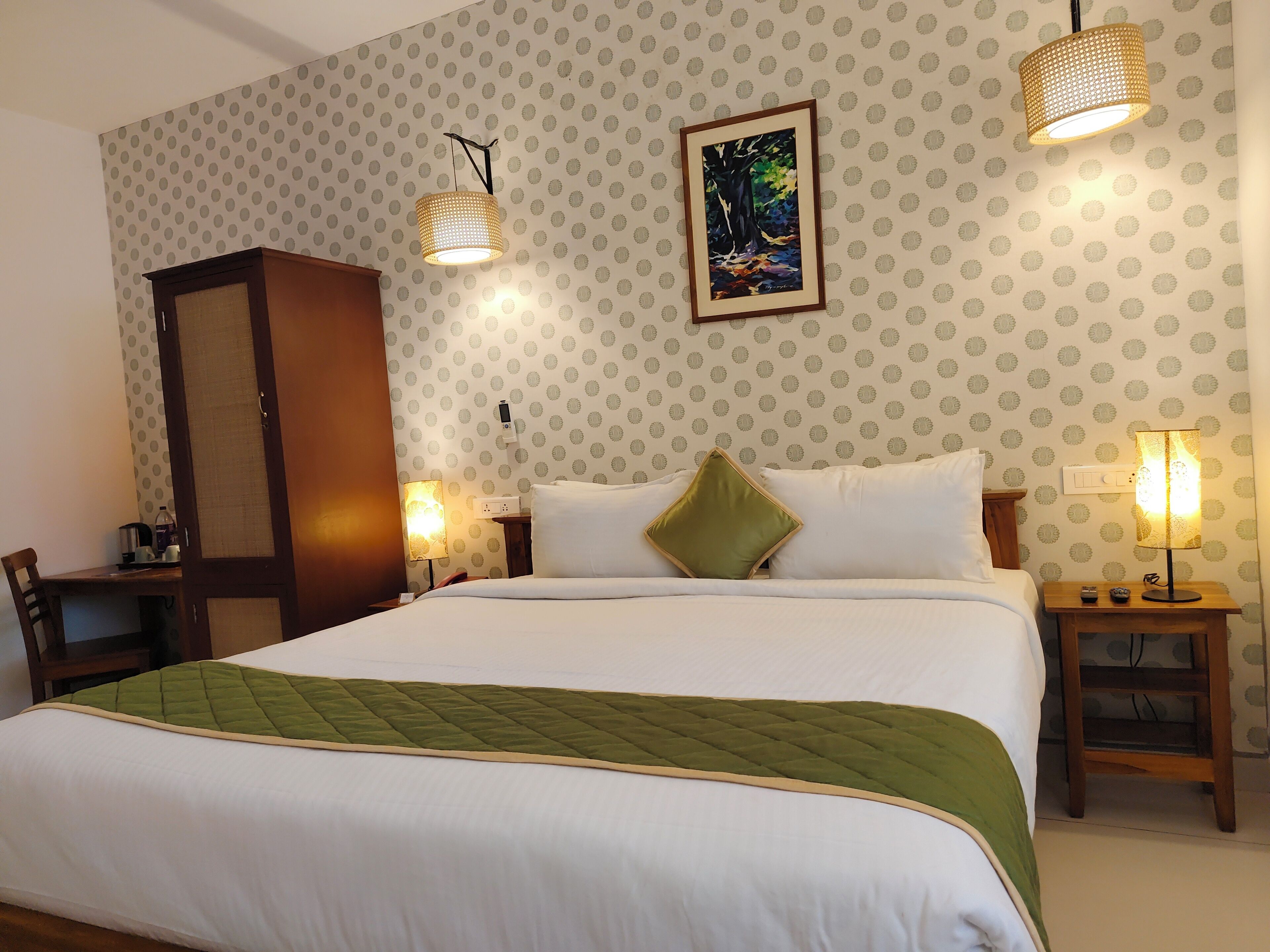 A hotel room with a large bed, two bedside lamps, a wardrobe, and a painting on the wall.