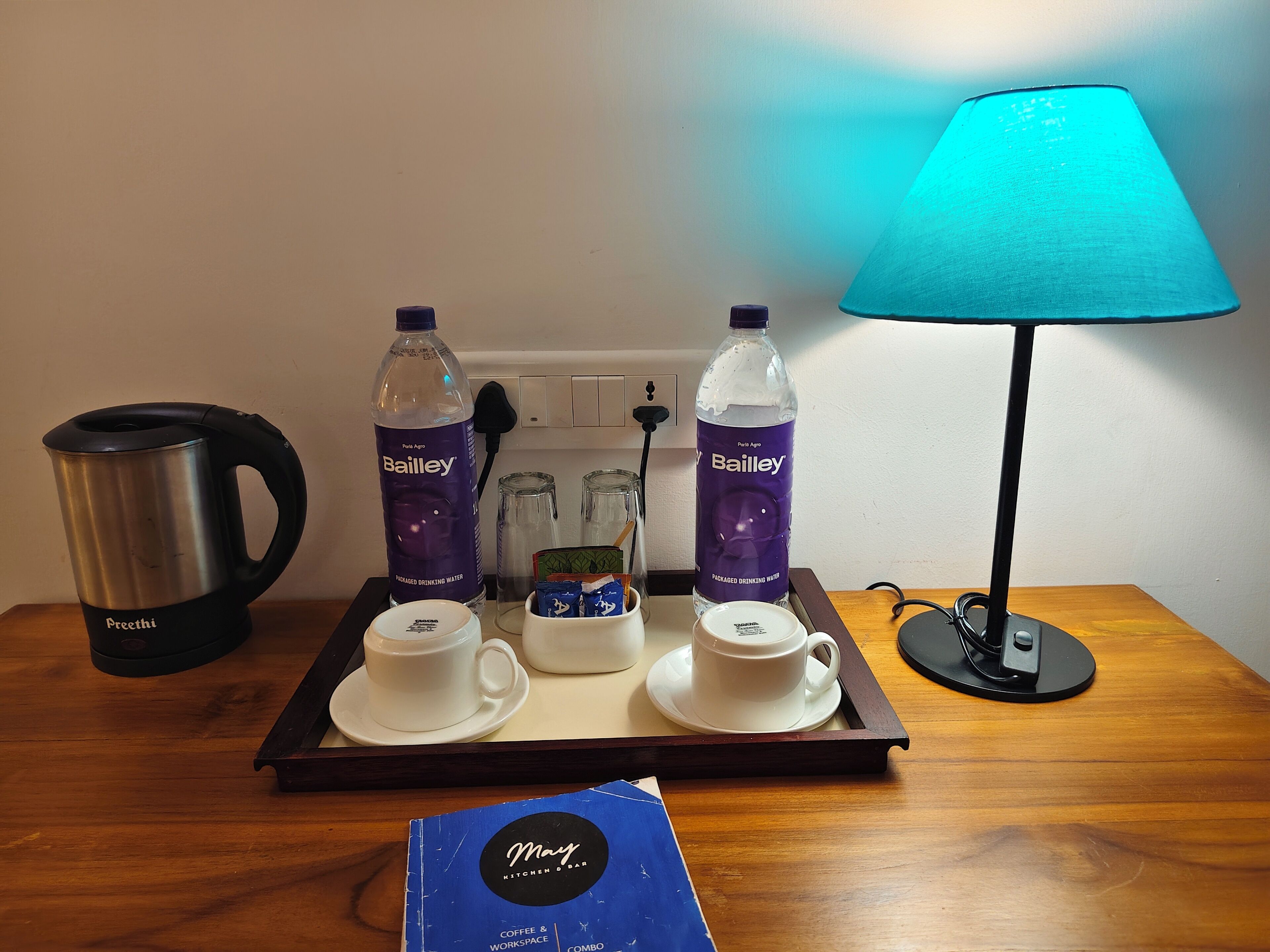 A tray with a Bailey water bottle, a kettle, two cups, and a tray on a wooden table.