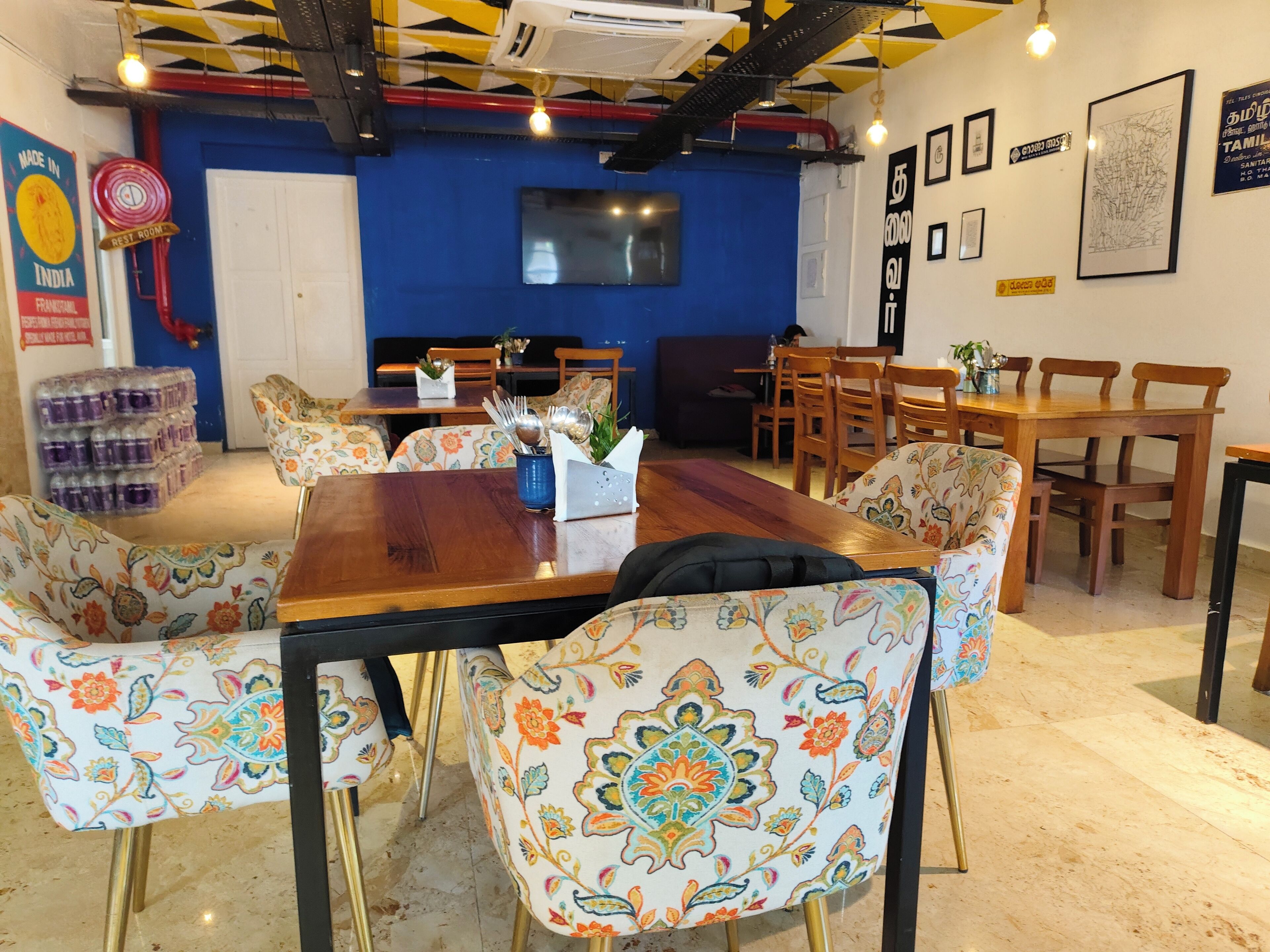 Una zona pranzo con tavolo in legno, sedie a motivi floreali, televisione e una parete azzurra.