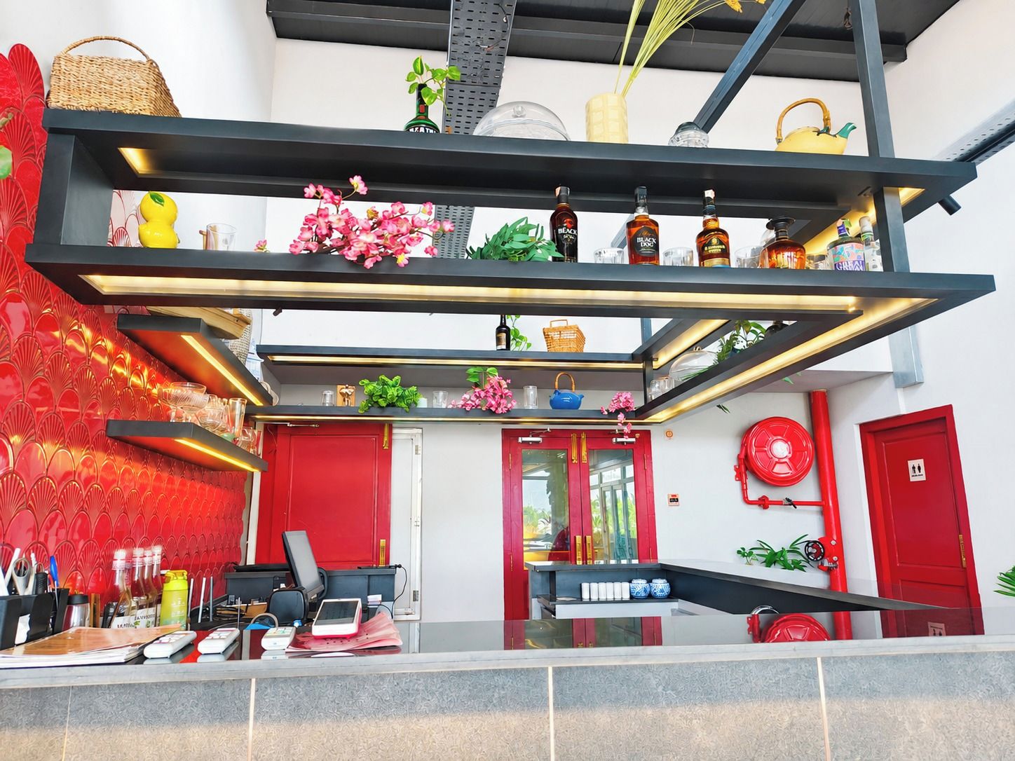 A modern interior with a reception desk, red doors, and a suspended shelf with various items.