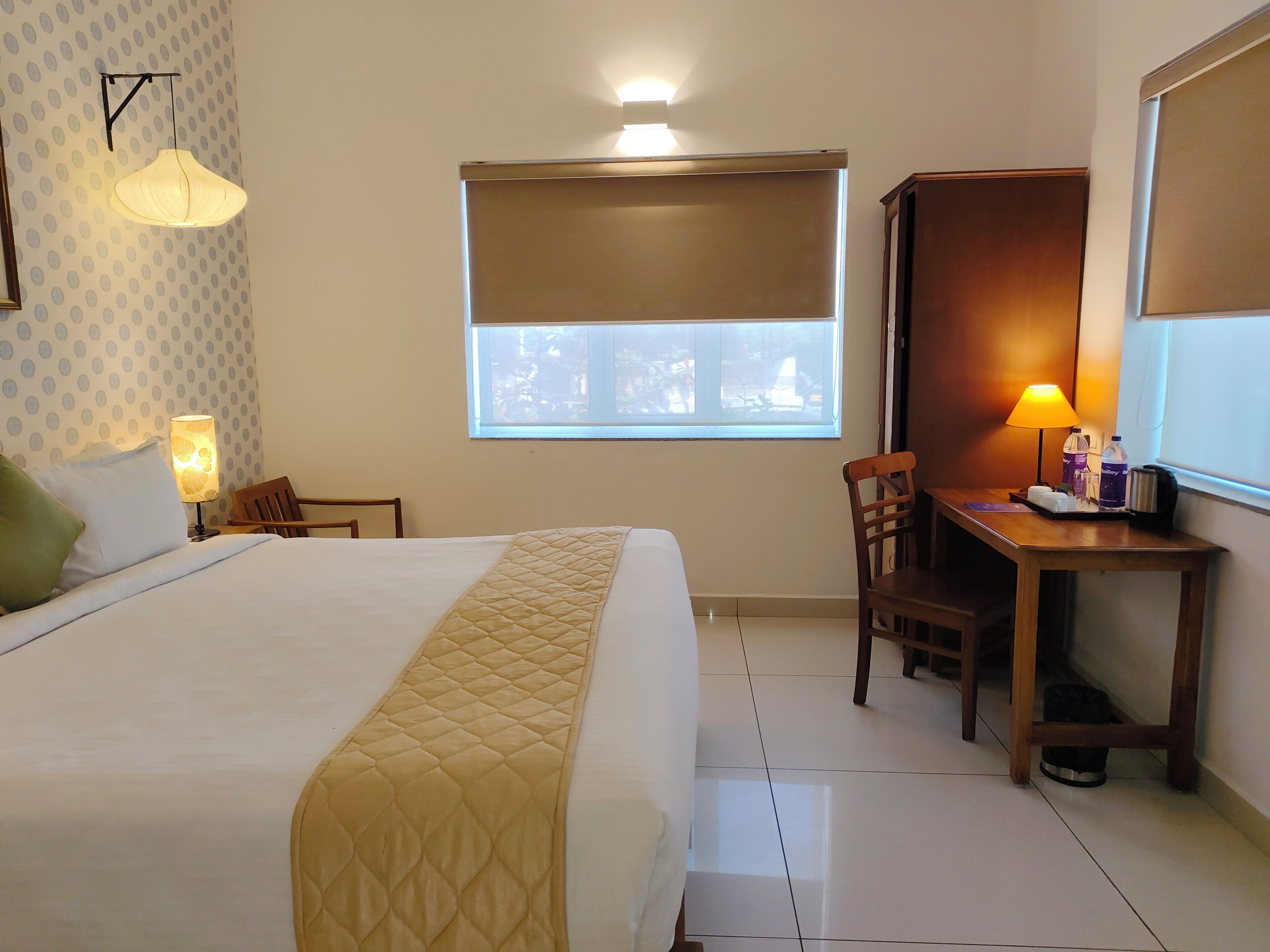 A hotel room with a bed, a desk, a chair, a lamp, and a window.