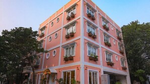 A multi-story building with balconies, large potted plants, and a sign that reads "AURA". - Hotel Aura by Woco Stays (Puducherry)