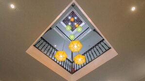 A high-ceiling atrium with a central skylight, geometric patterned ceiling, and a staircase with black railings. - Hotel Aura by Woco Stays (Puducherry)