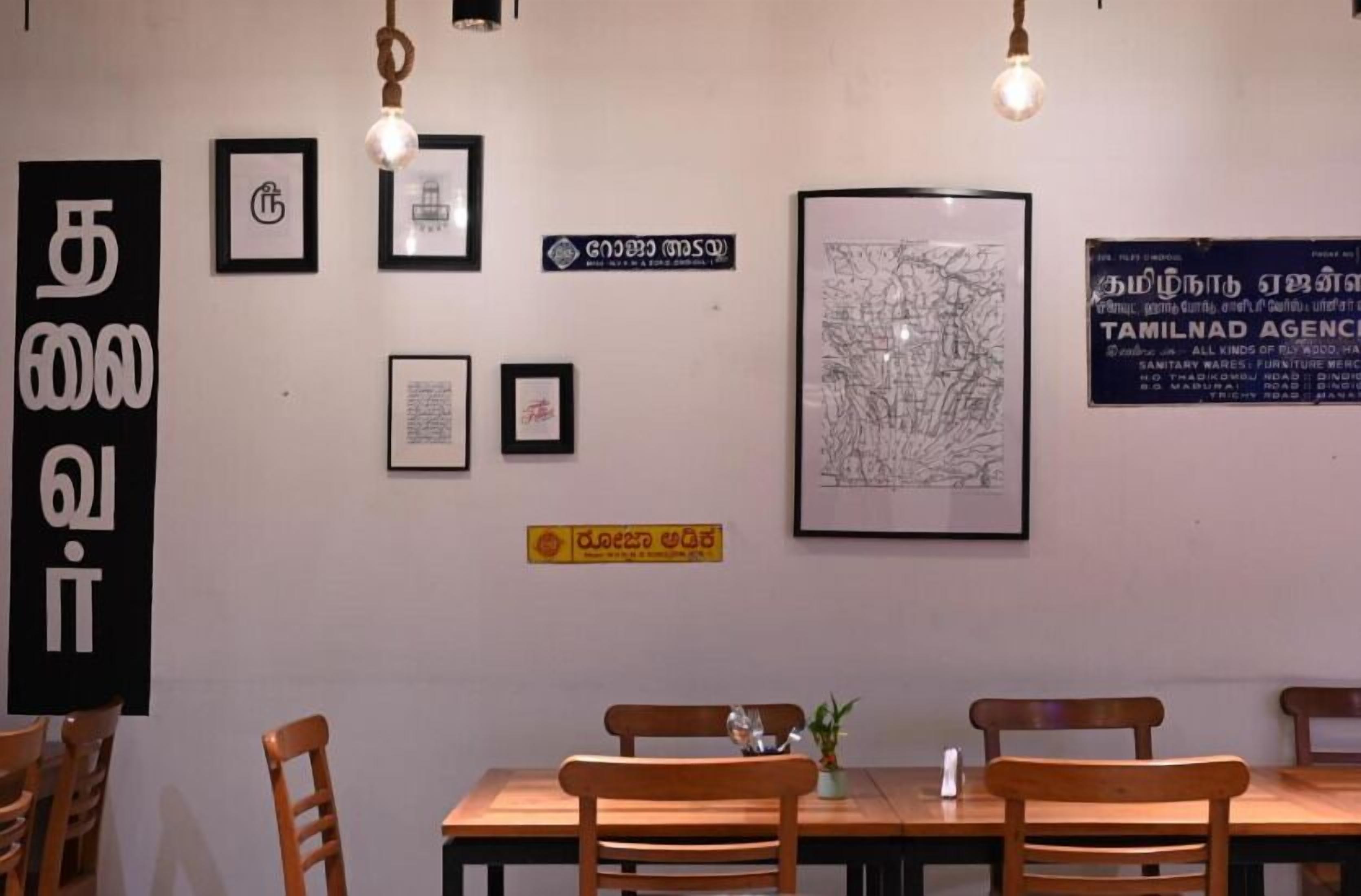 A restaurant interior with wooden tables and chairs, framed artwork on the walls, and hanging light fixtures.