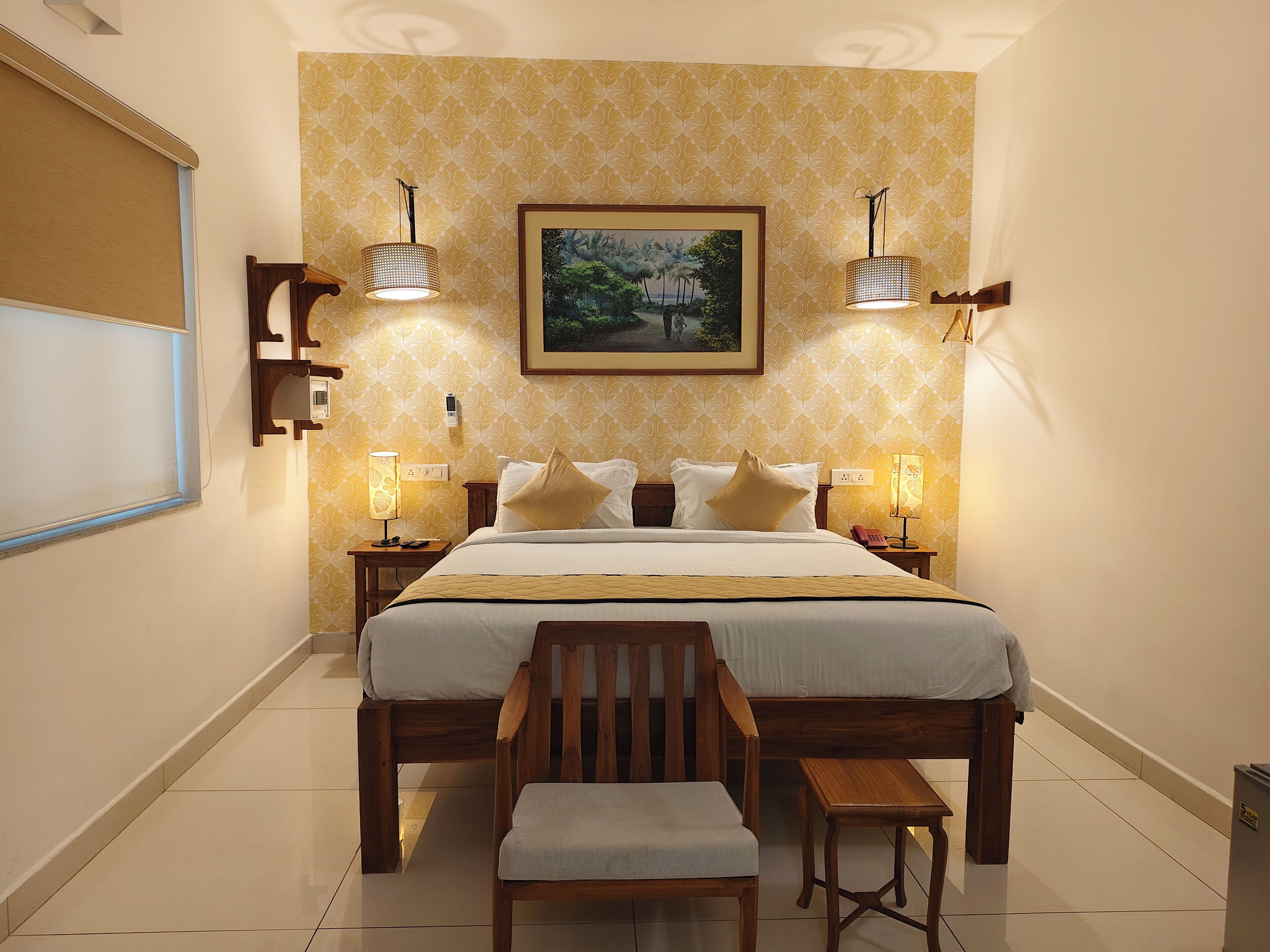 A hotel room with a large bed, two bedside lamps, a wooden chair, a small table, and a framed picture on the wall.