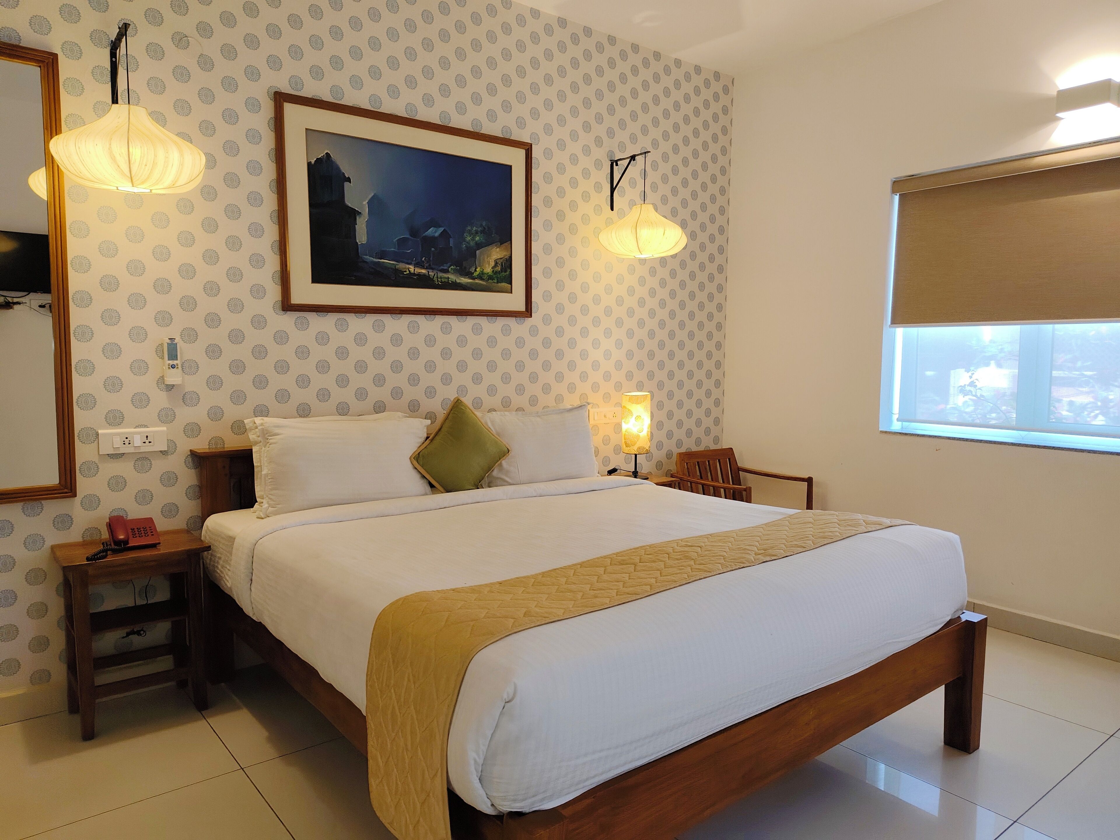 Una camera da letto ordinata con un letto, lampade da comodino, un comodino, un telefono, un quadro appeso al muro e una finestra con vista.