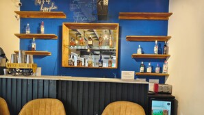 A bar area with a blue wall, wooden shelves with bottles, a mirror, and two yellow chairs. - Hotel Aura by Woco Stays (Puducherry)