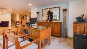 A spacious living area with a wooden coffee table, chairs, a large mirror, and a stone pillar. - Hotel Aura by Woco Stays (Puducherry)