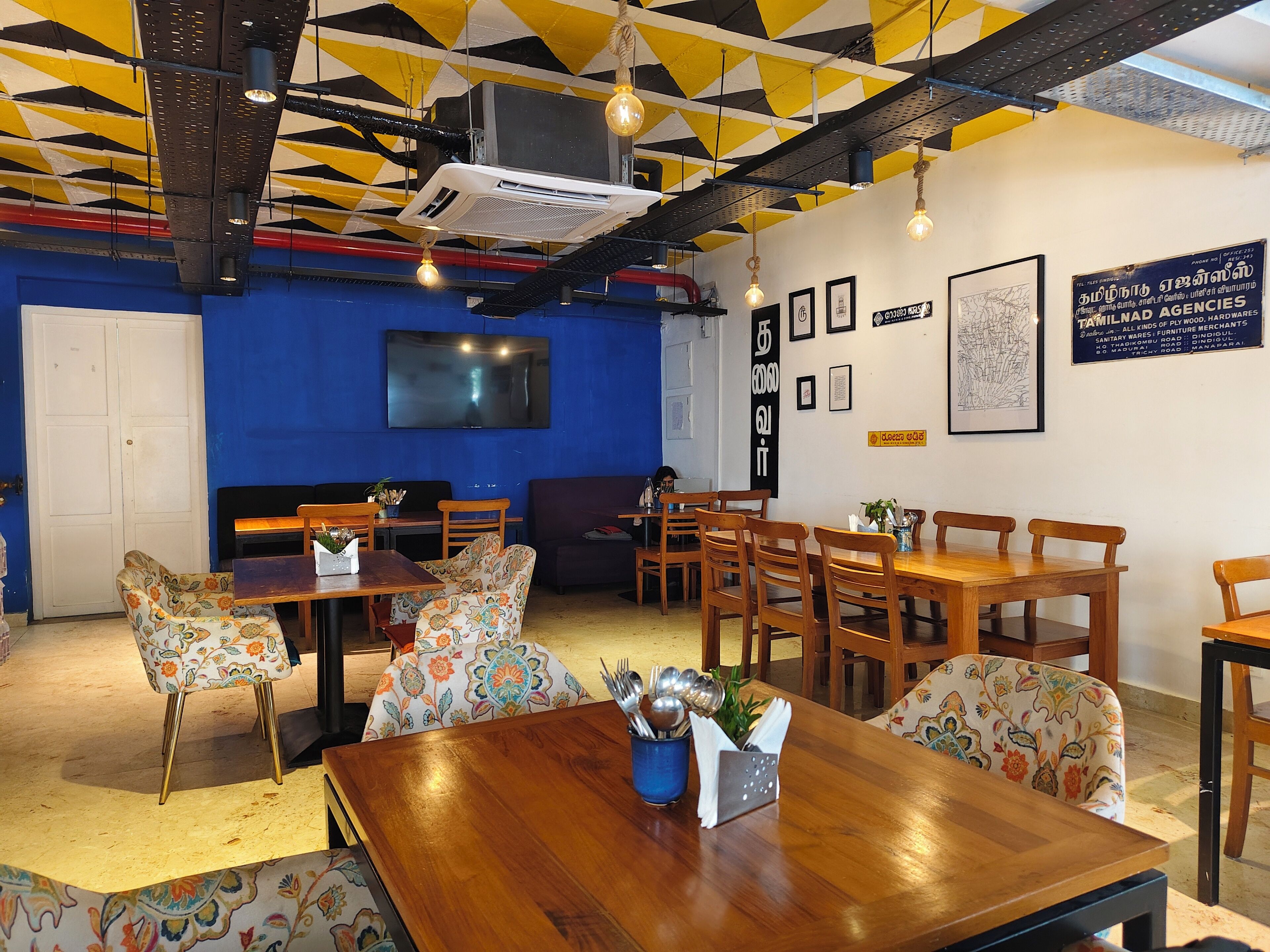 A modern interior with a blue accent wall, a large flat-screen TV, and a variety of seating options including wooden tables and patterned chairs.