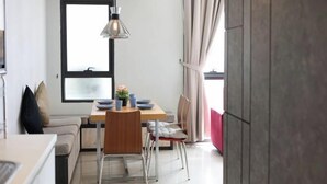 Un espacio habitable compacto con comedor, kitchenette y un amplio ventanal con cortinas.
