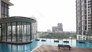 Piscina infinita en la azotea con cubierta de madera y sillas de descanso, rodeada de edificios altos.