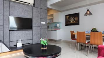 A modern living room with a flat-screen TV, a round black table with a potted plant, and a dining area with wooden chairs and a table.
