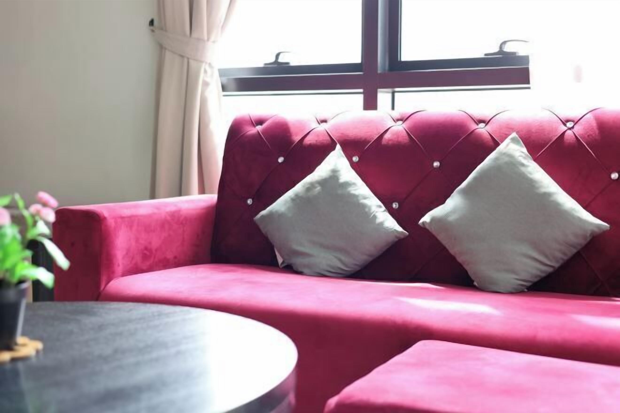 A red sofa with two white cushions, a round table, and a window with curtains.