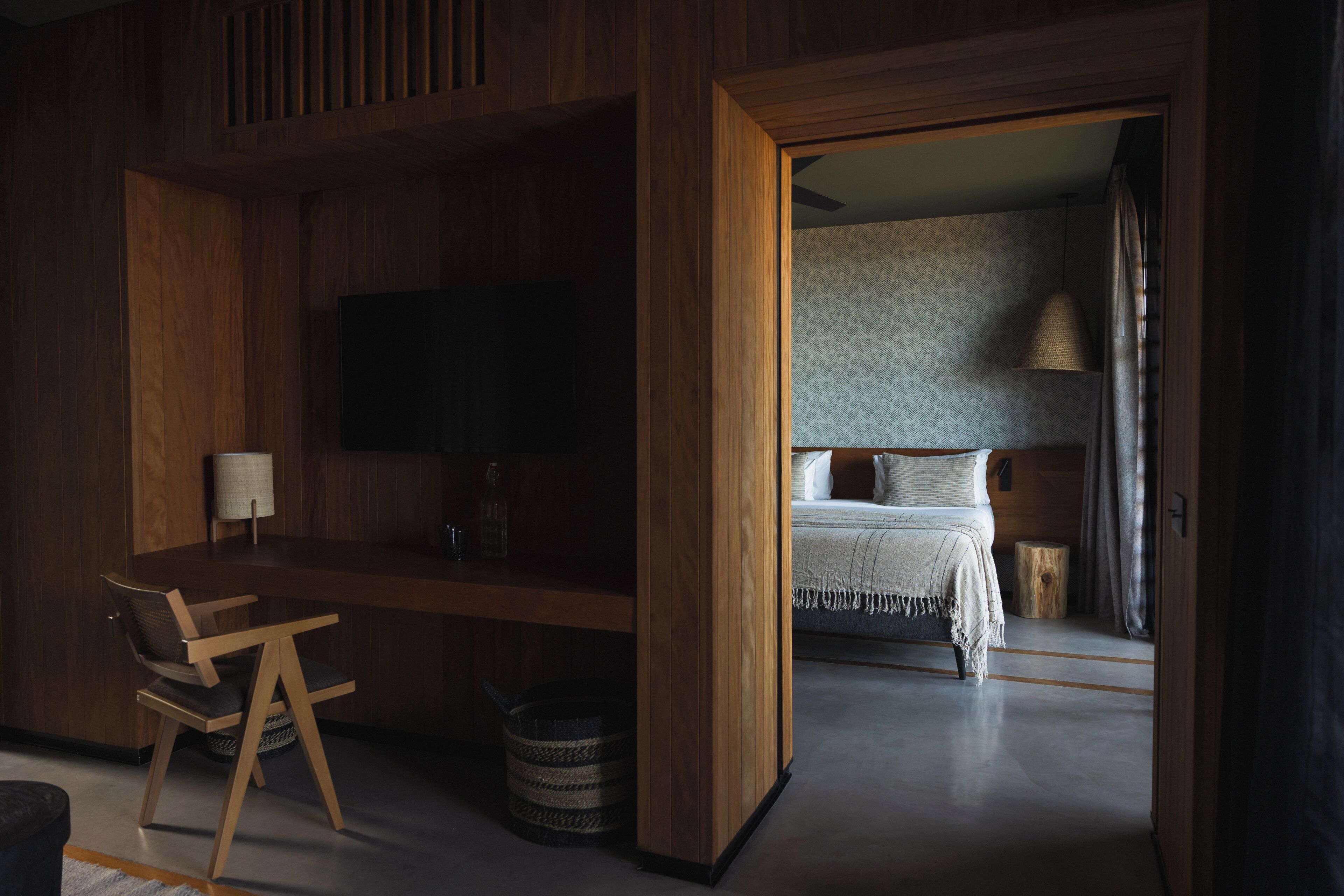 A modern room with a wooden desk, a television, a bed with a headboard, and a small round table.