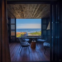 Um deck de madeira com duas cadeiras e uma pequena mesa, com vista para a costa.