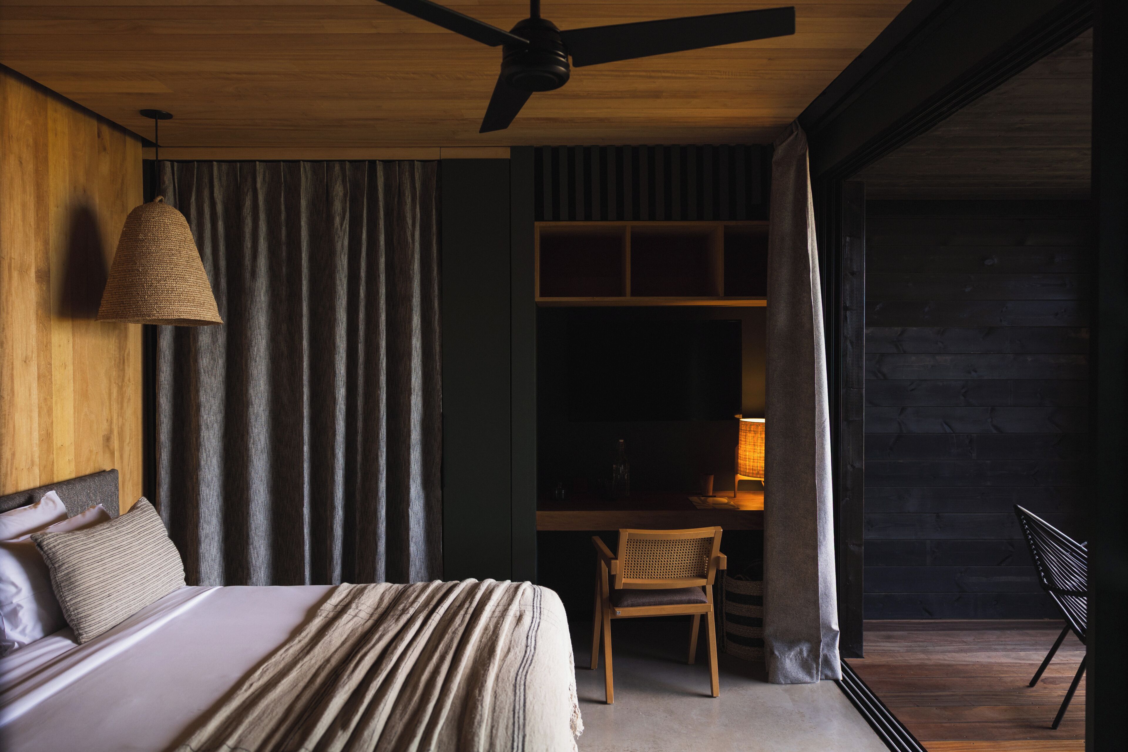 Une chambre à coucher comprenant un lit, un bureau, une chaise, un ventilateur de plafond et une fenêtre avec des rideaux.