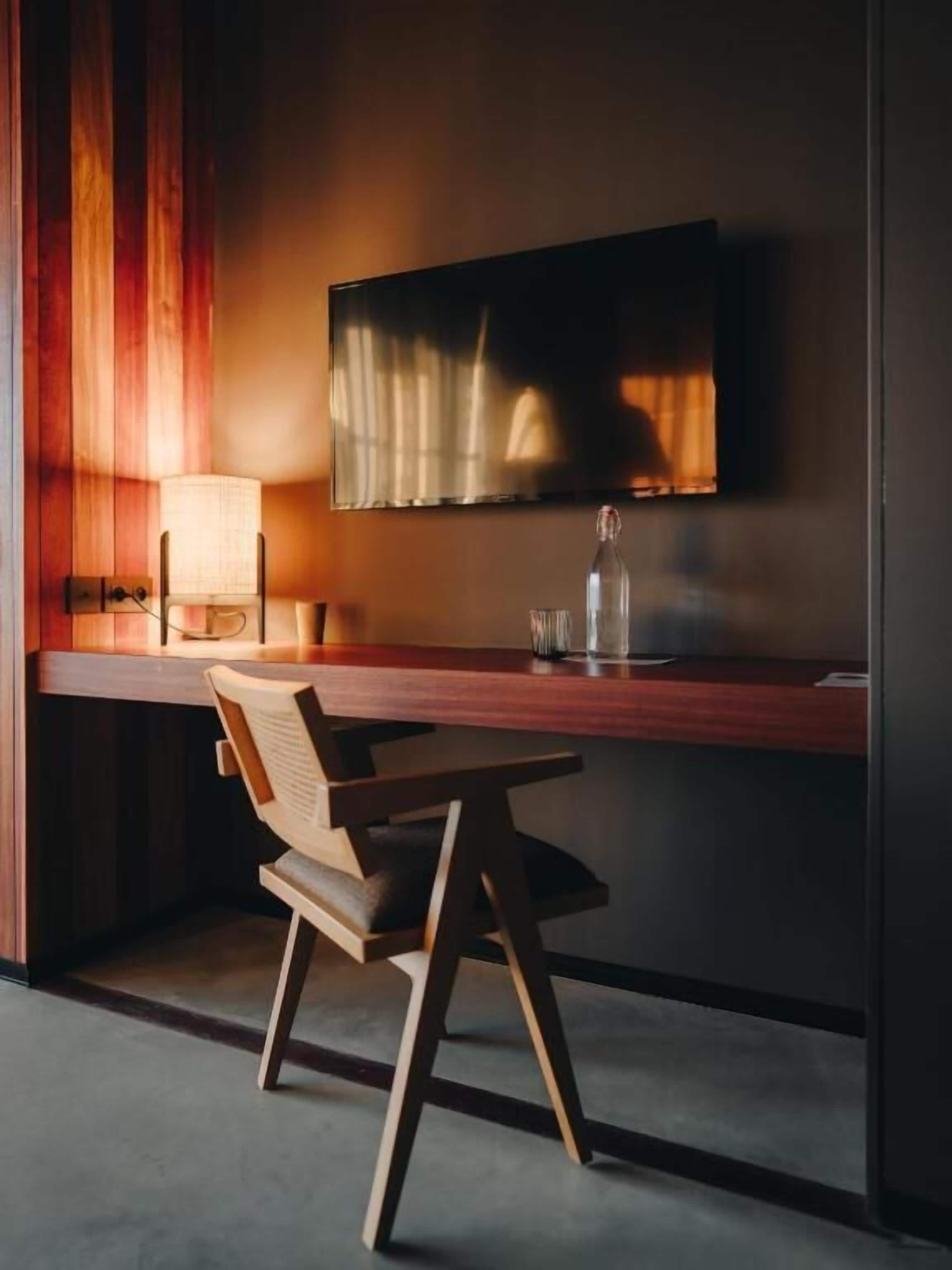 A modern kitchen with a wooden countertop, a chair, a table, and a television mounted on the wall.
