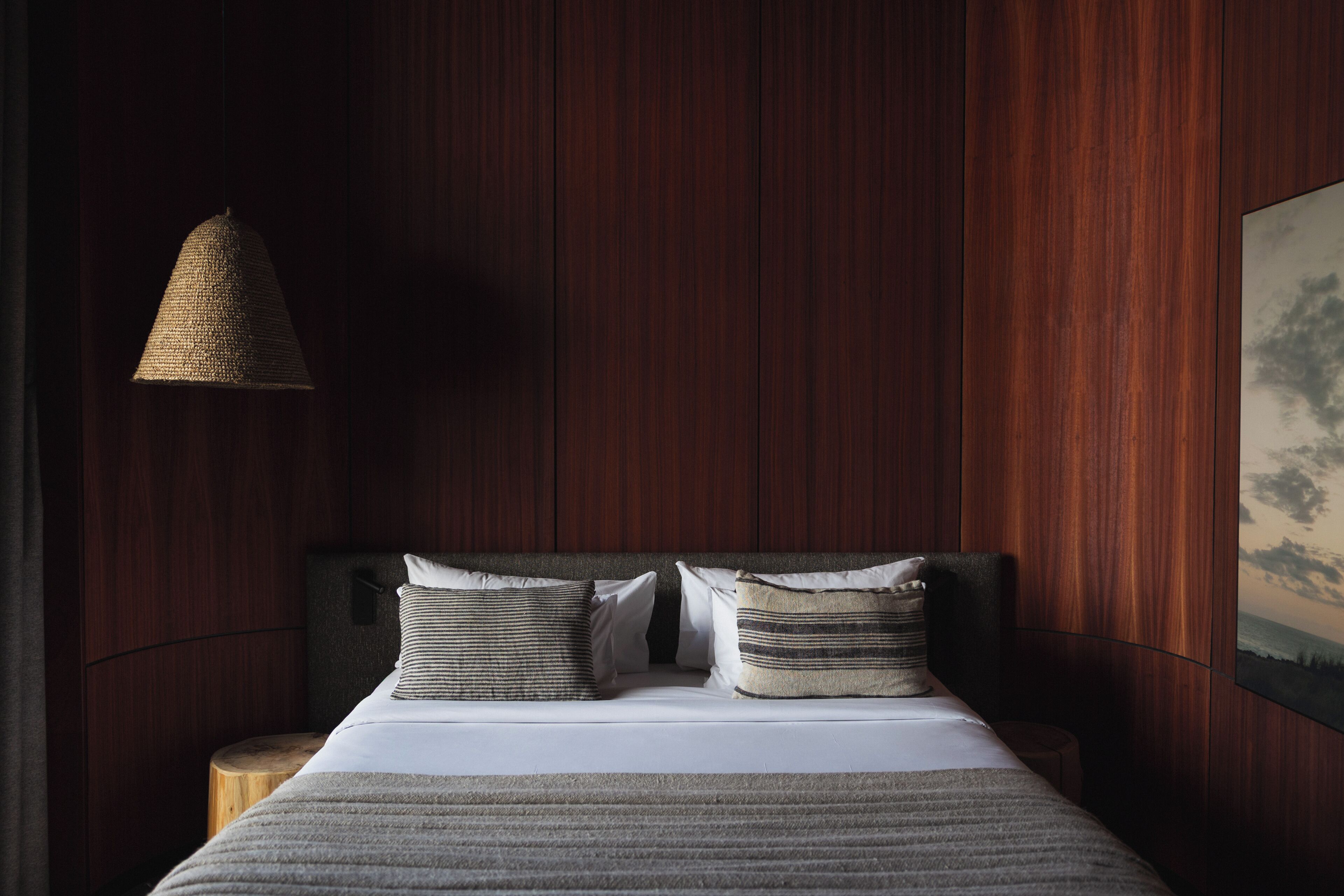 Une chambre à coucher comprenant un lit, deux oreillers, une table de chevet, une lampe suspendue et un tableau accroché au mur.