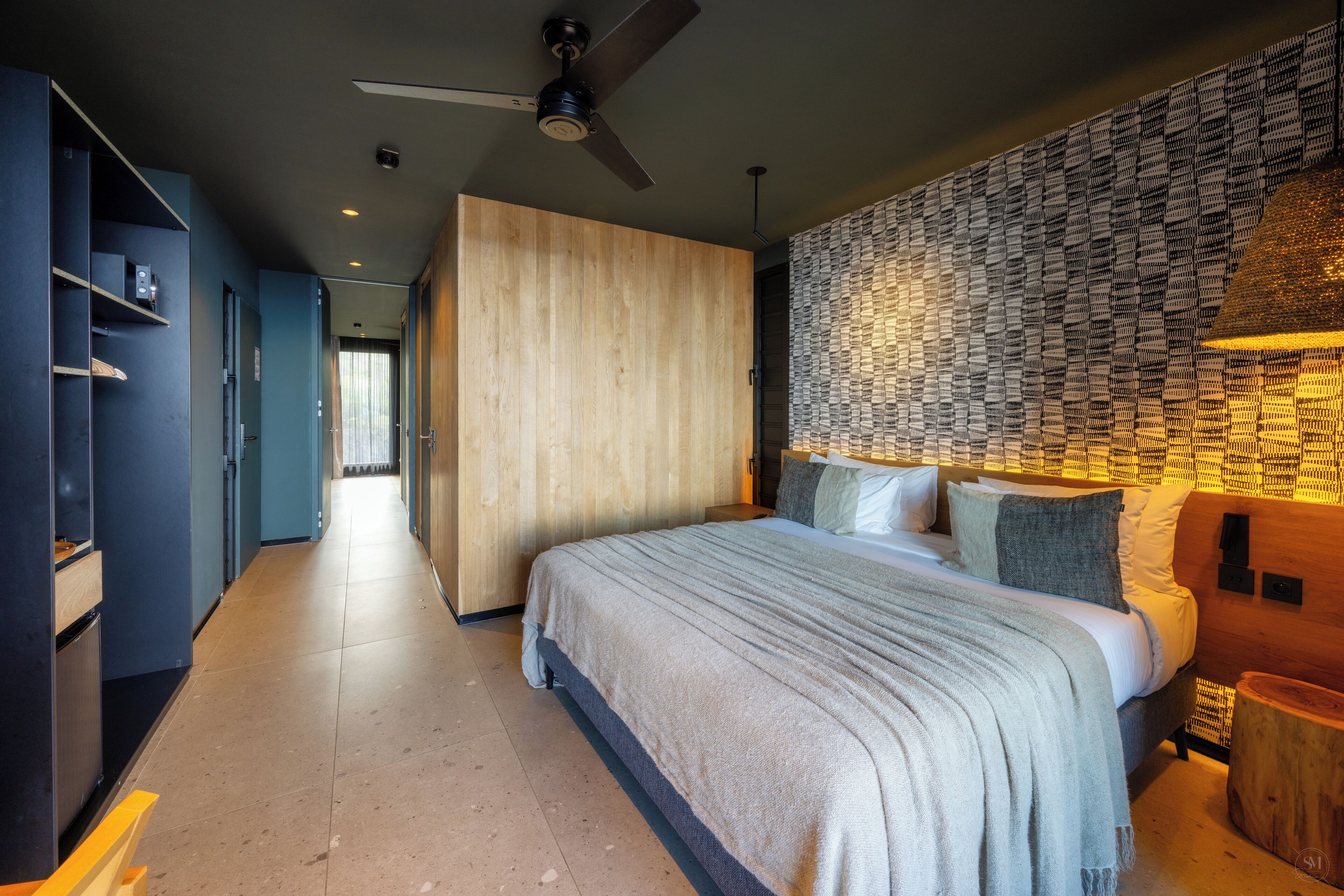 Ein modernes Hotelzimmer mit einem großen Bett, einem Deckenventilator, einem Holzschrank und einer Wand mit Muster.