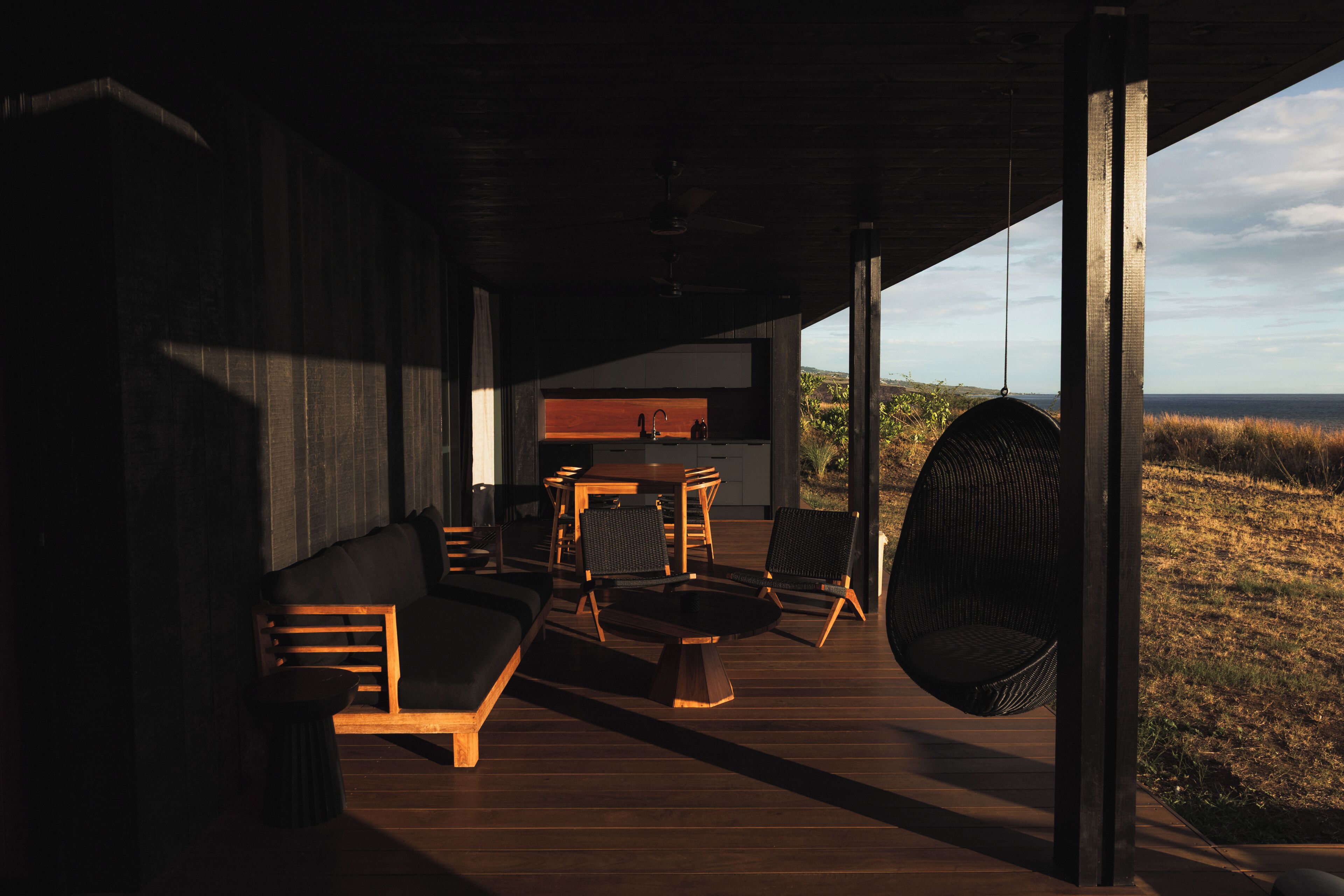 An interior with a wooden floor, a sofa, a dining table, chairs, and a hanging chair.