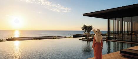 A person standing by a pool with a view of the ocean and a modern building.