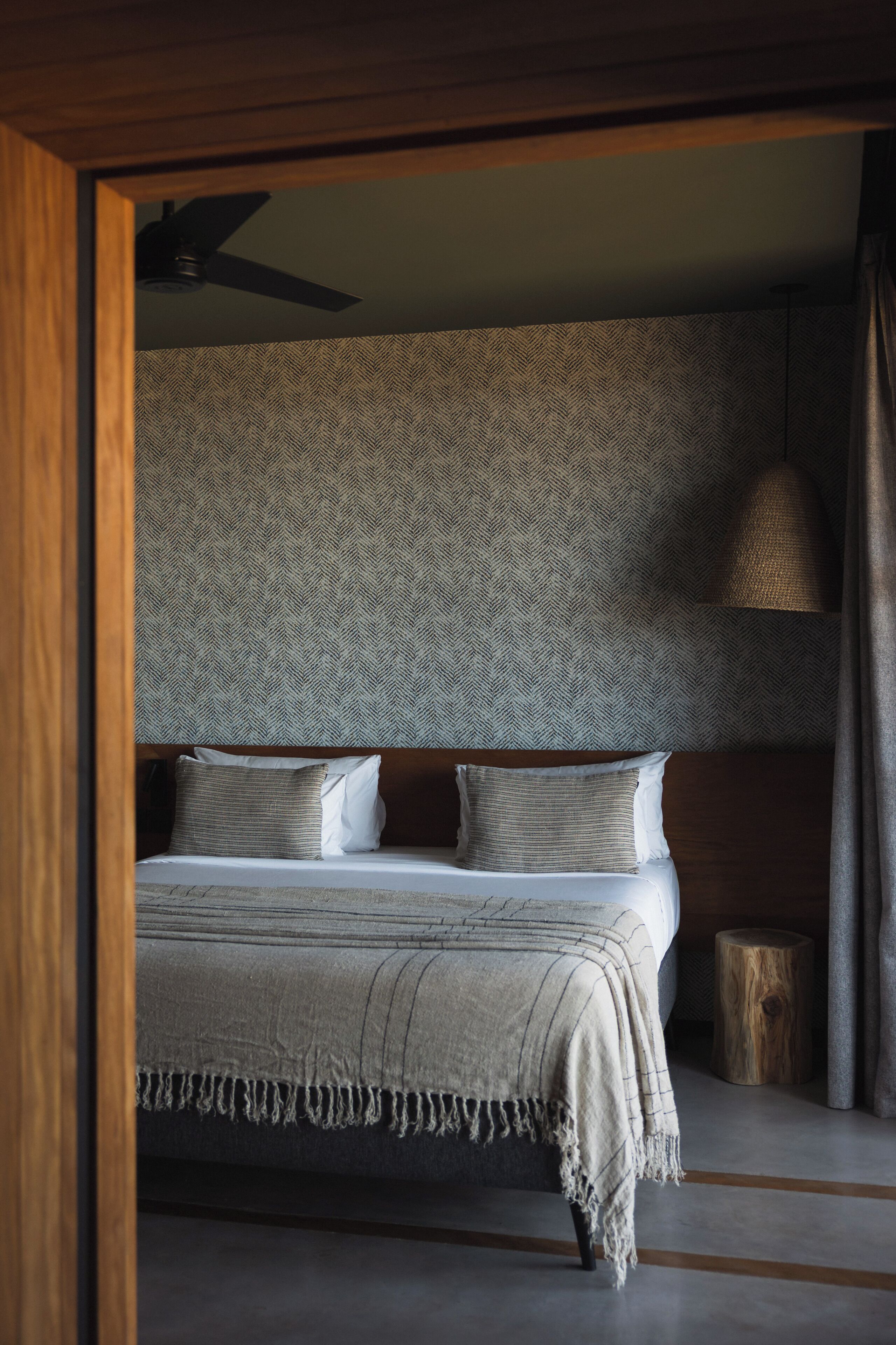 Un dormitorio con cama, ventilador de techo, pared texturizada y suelo de madera.
