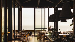 A restaurant with a view of the sea, wooden tables and chairs, and hanging pendant lights. - WOOD HOTEL & SPA (Trois-Bassins)