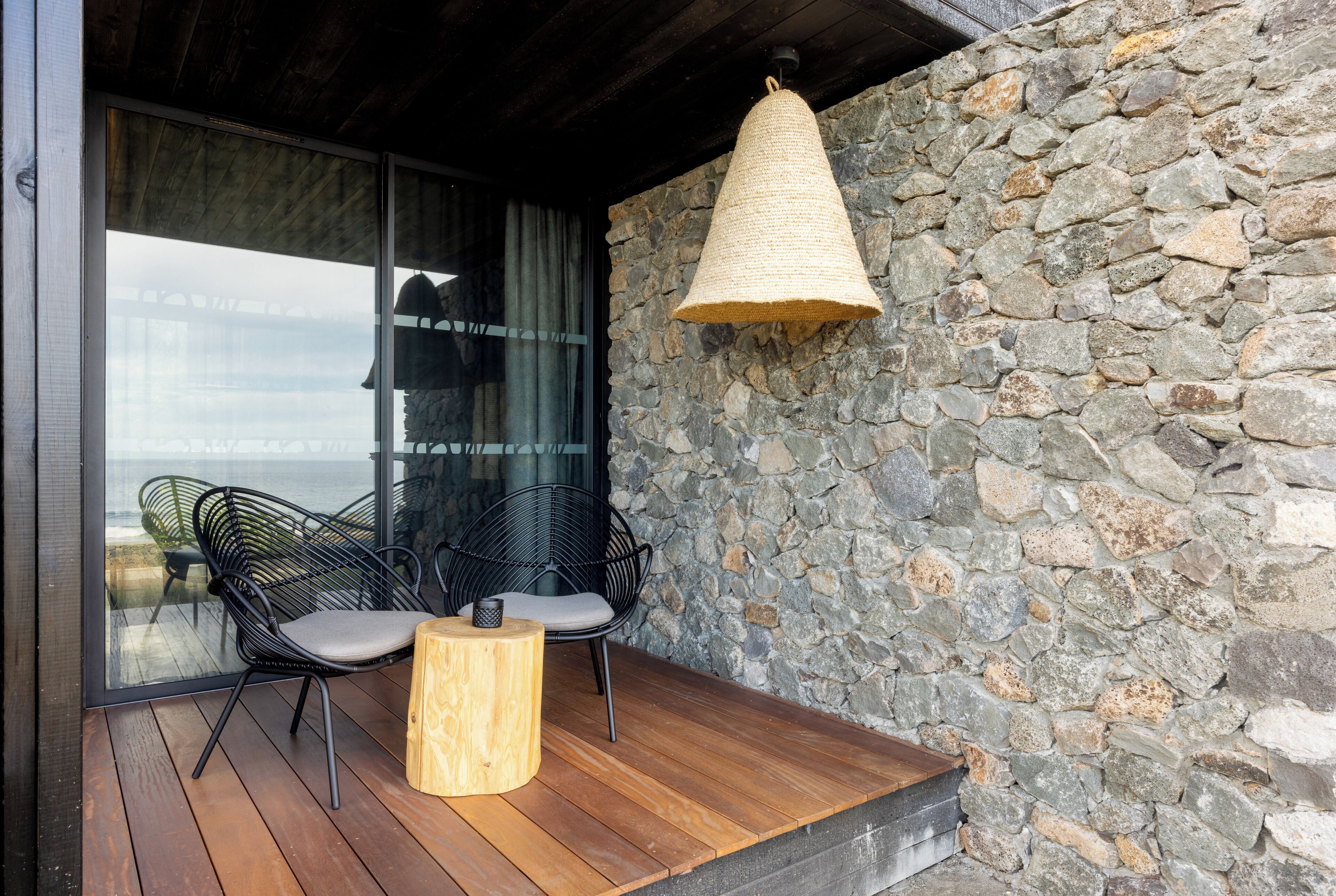 A wooden deck with two black wire chairs and a woven light fixture.