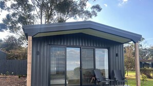 A modern outdoor structure with a covered patio, large sliding glass doors, and a seating area with chairs.