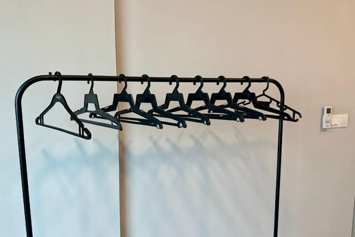 A metal coat rack with multiple hangers against a plain wall.