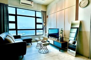 Ein modernes Hotelzimmer mit großem Fenster, einer Couch, einem Fernseher, einem Spiegel und einer Wanduhr.
