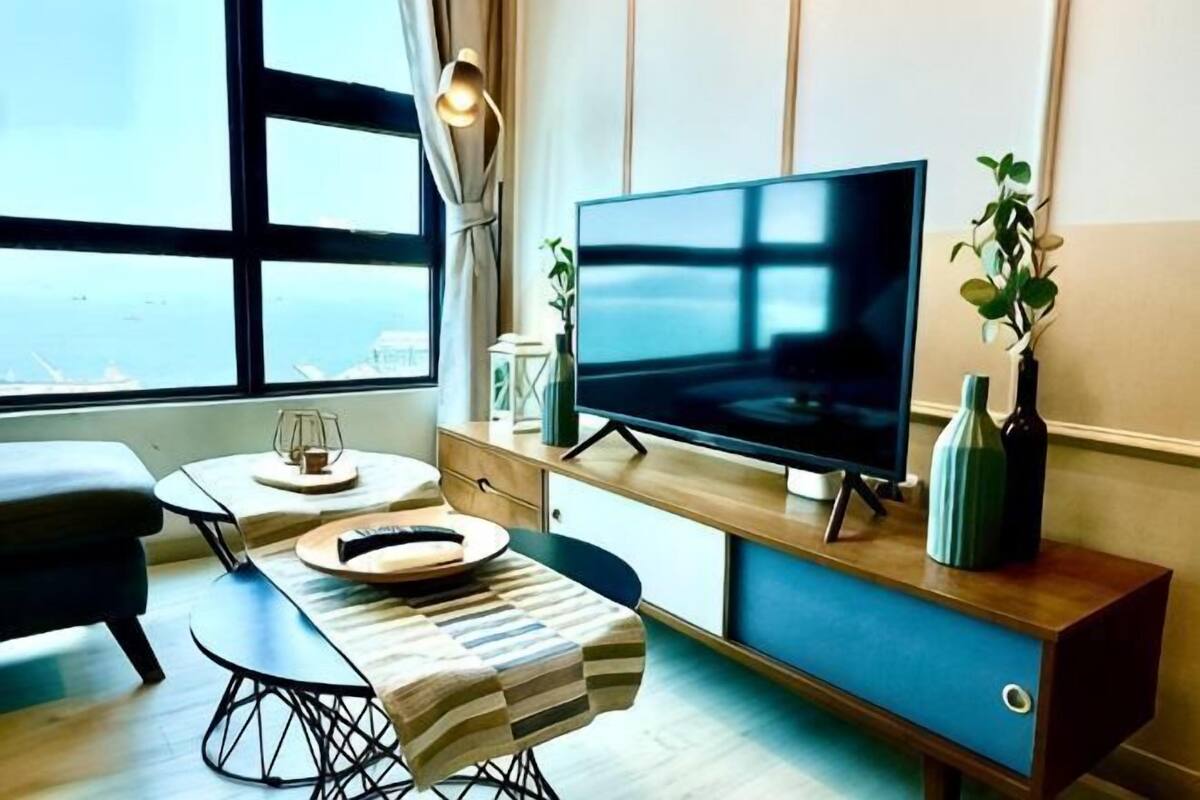 Ein modernes Wohnzimmer mit großem Flachbildfernseher, einem Esstisch mit Stuhl, einer Couch und Meerblick durch ein großes Fenster.