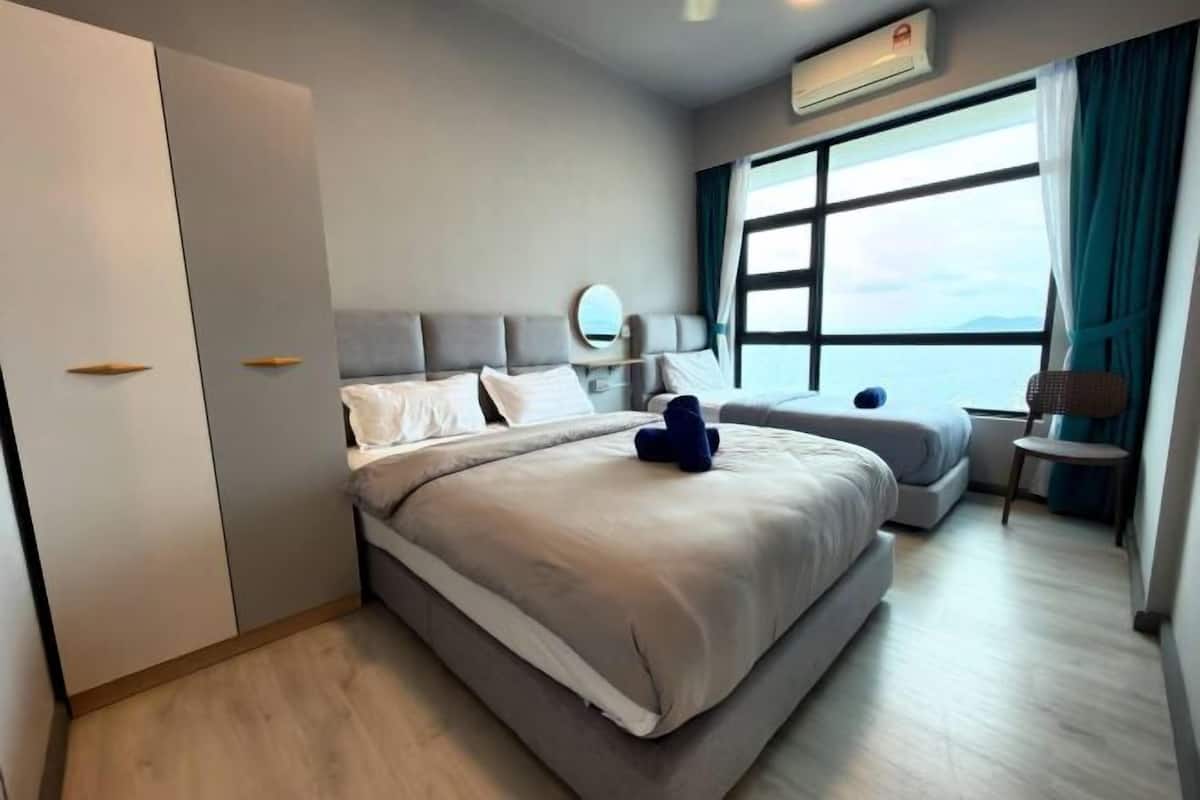 Ein modernes Hotelzimmer mit einem großen Bett, einer kleinen Sitzecke, einem Sessel und Meerblick.