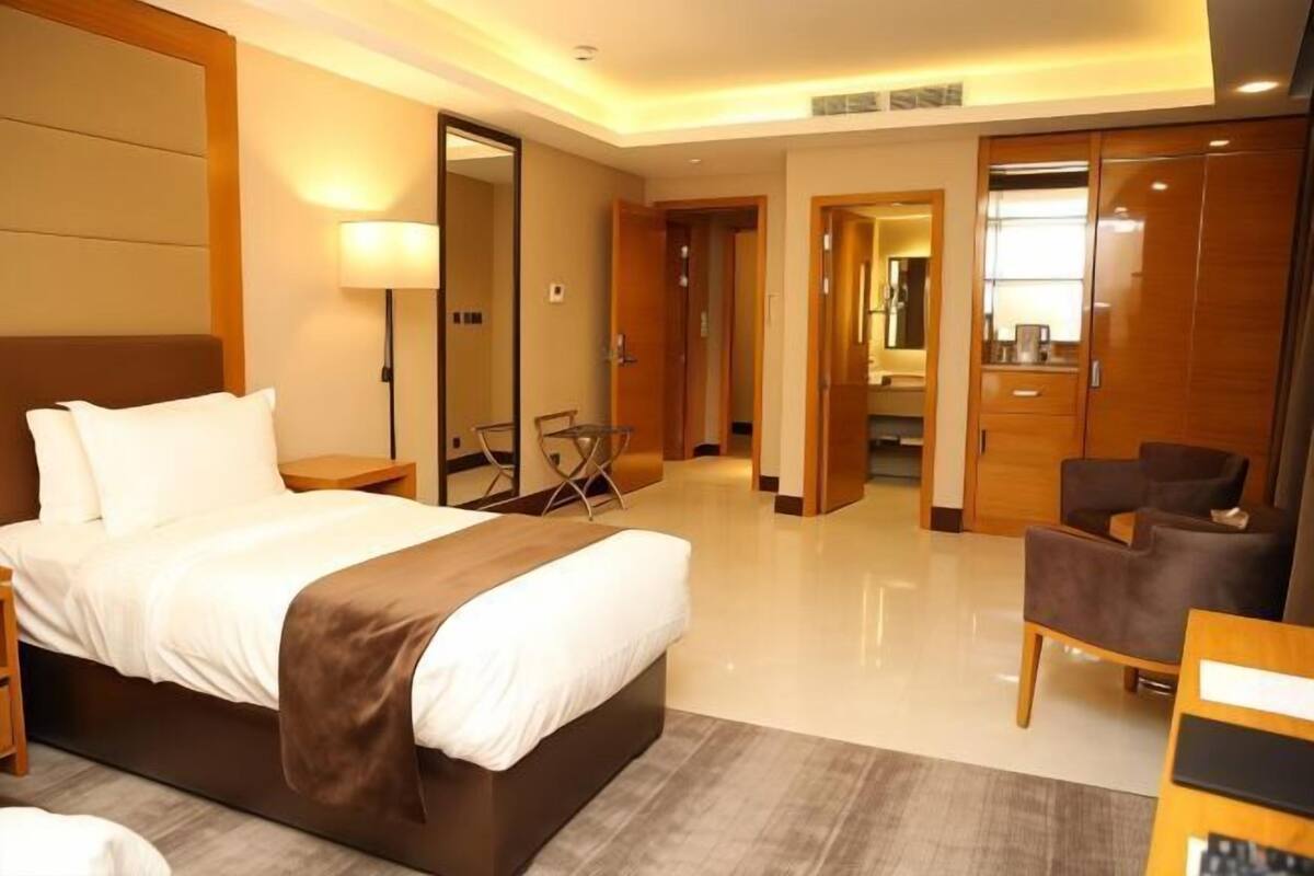 A hotel room with a bed, a desk, a chair, a wardrobe, and a mirror.