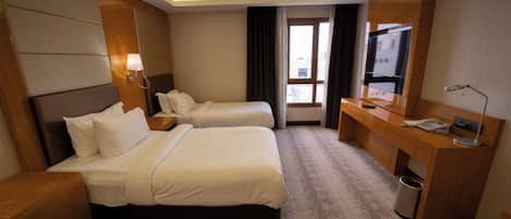 A hotel room with two beds, a desk, a TV, and a window with curtains.