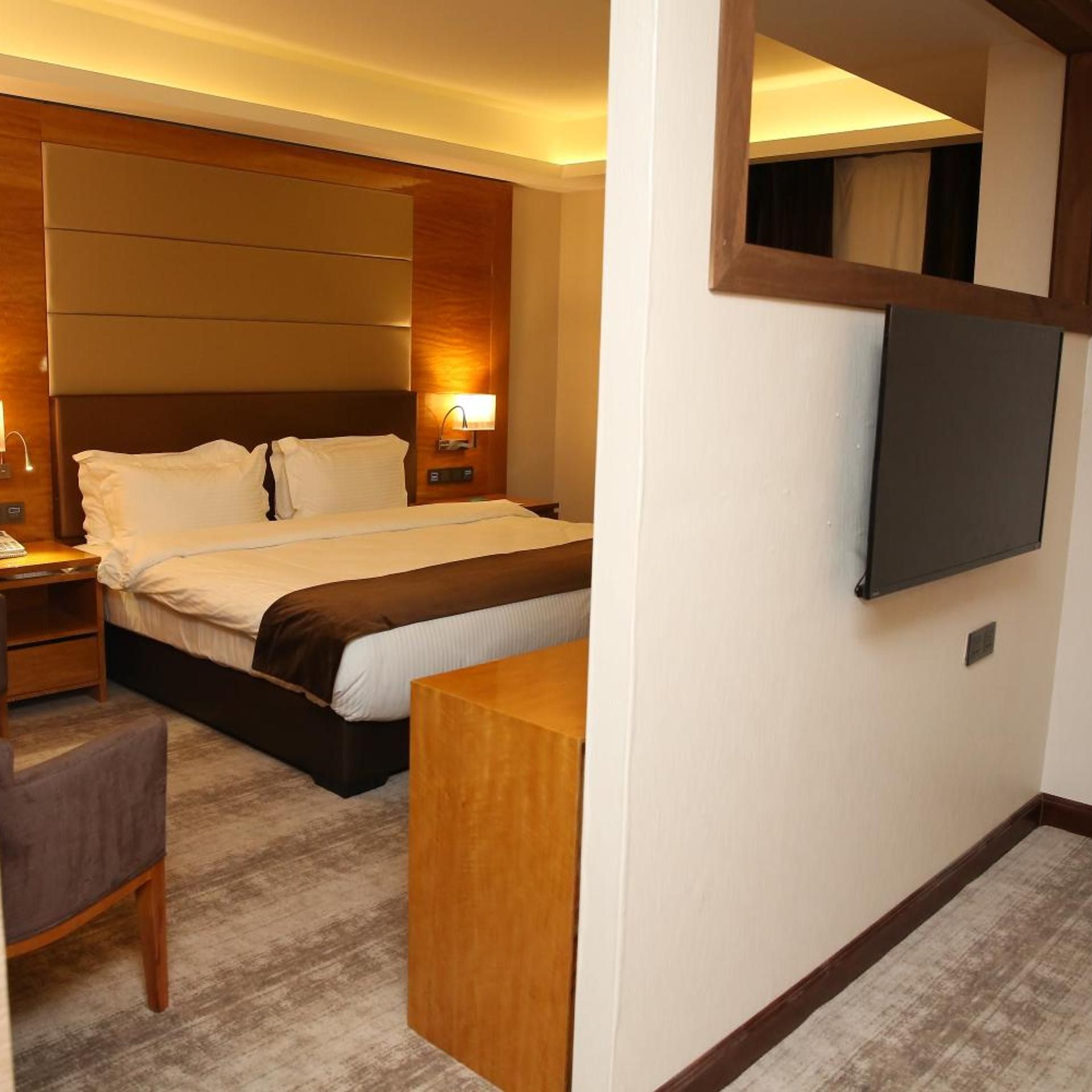 A hotel room with a bed, bedside table, chair, and a flat-screen TV mounted on the wall.