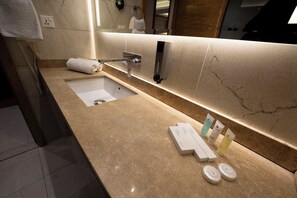 A modern bathroom with a marble countertop, a sink, a towel rack, and a mirror. - Gloria Hotel (Amman)